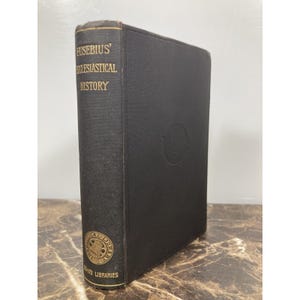 May include: A hardcover book titled "Eusebius' Ecclesiastical History" with gold lettering on a black cover. The book has a gold emblem on the spine and a circular emblem on the front cover. The book is from the "Loeb Classical Library".