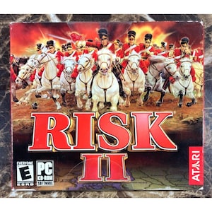 May include: A PC CD-ROM game box for Risk II. The cover art features a painting of soldiers on white horses charging forward. The game title is in large red letters. The ESRB rating is visible.
