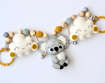 May include: A gray felt koala with white ears and a white belly hangs from a wooden and felt garland. The garland features yellow and white clouds with smiling faces and wooden beads.