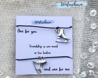May include: Two black elastic bracelets with silver ice skate charms. The bracelets are on a white card with the text "One for you" and "Friendship is one mind in two bodies" and "and one for me".