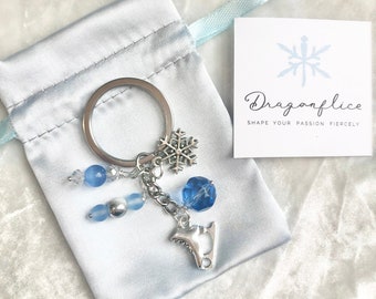 Peut inclure: Un porte-clés argenté avec un charm en forme de flocon de neige, des perles bleues et un charm en forme de patin à glace. Le porte-clés est présenté avec une petite pochette en satin et une carte avec le texte "Dragonflice".