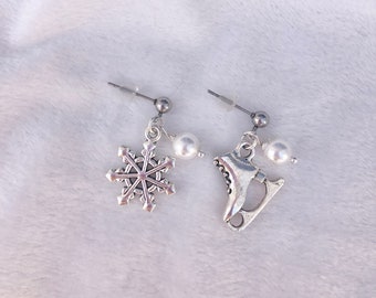 Peut inclure: Une paire de boucles d'oreilles en argent avec un charme flocon de neige et un charme patins à glace en argent sur une boucle d'oreille et une perle sur l'autre.