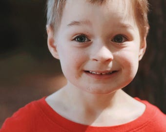 May include: A child wearing a red t-shirt with the text "THE AMAZING" and a butterfly crown. The butterfly crown features a realistic orange and black butterfly and green leaves. The child is smiling.