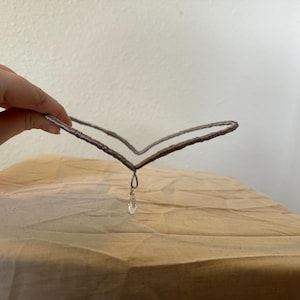 May include: A silver wire headband with a teardrop-shaped crystal pendant.