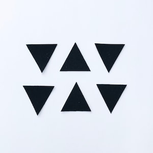 Peut inclure: Six triangles en feutre noir disposés de manière symétrique sur un fond blanc.