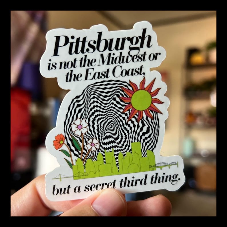 May include: A white sticker with black text that reads "Pittsburgh is not the Midwest or the East Coast, but a secret third thing." The sticker features a black and white swirling design with a yellow sun and green flowers.