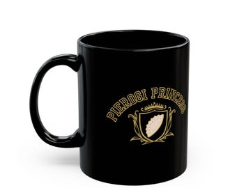 May include: Black ceramic mug with a curved handle. The mug features the words "PIEROGI PRINCESS" in gold lettering above a gold crest with a pierogi illustration.