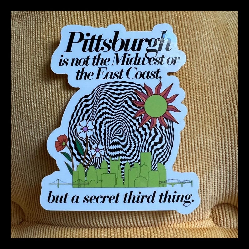 May include: A white sticker with black text that reads "Pittsburgh is not the Midwest or the East Coast, but a secret third thing." The sticker features a black and white swirling design with a green sun and green city skyline.