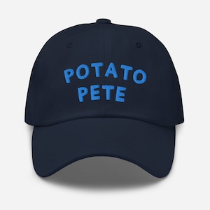 May include: Navy blue baseball cap with the embroidered text "POTATO PETE" in light blue. The cap has a curved brim and a six-panel design, suitable for casual wear.