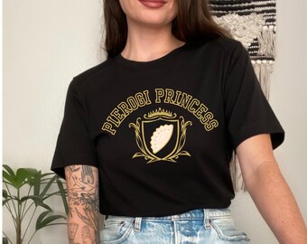 May include: Black t-shirt with gold lettering that reads "Pierogi Princess" and a gold crown above a shield with a pierogi inside.