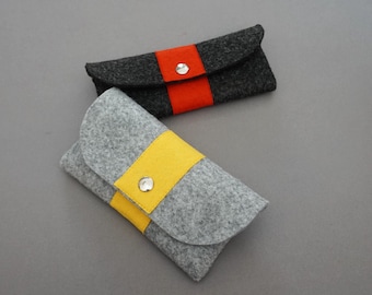 May include: Two felt pencil cases, one gray with a yellow stripe and one black with a red stripe. Both cases have a silver button closure.