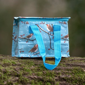 May include: A blue lunch bag with a white background and a pattern of robins and red berries. The bag has two blue handles.