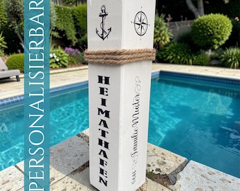 May include: A white wooden pillar featuring a black anchor and compass graphic, wrapped with a thick jute rope. The text "HEIMATHAFEN" is printed vertically in black, alongside the script text "von Familie Muster" on the side.