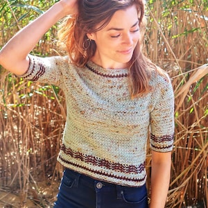May include: A light green crochet top with brown and white accents. The top has short sleeves and a round neckline.