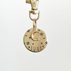 May include: Gold-toned pet tag with a crescent moon and star design. The tag is engraved with the word "LUNA" in a black font.