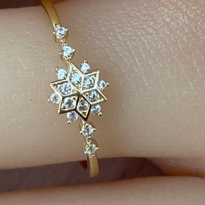 May include: A gold ring with a snowflake design set with clear cubic zirconia stones.