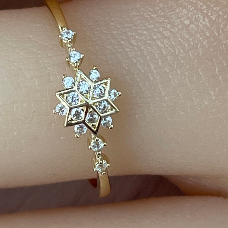 May include: A gold ring with a snowflake design set with clear cubic zirconia stones.