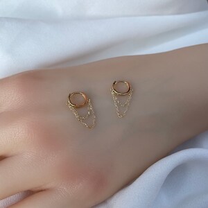 May include: A pair of gold hoop earrings with dangling chains. The hoops are small and the chains are delicate.