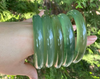May include: Set of four jade green bangle bracelets. The bracelets are stacked on top of each other and are smooth and polished.
