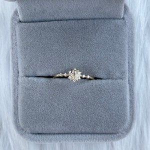 May include: A delicate gold ring with a snowflake design set with small diamonds. The ring is displayed in a gray velvet ring box.