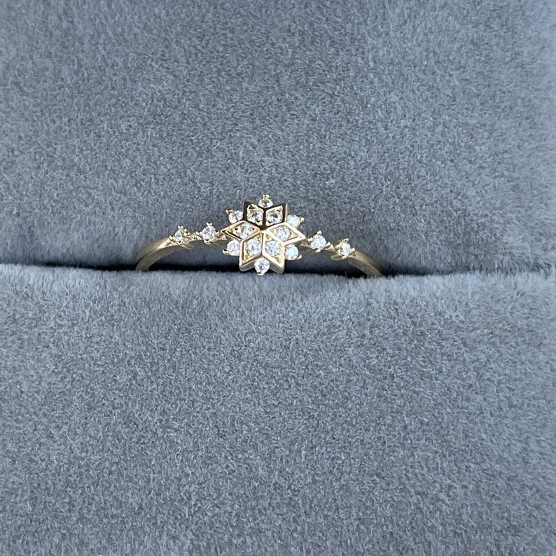 May include: A delicate gold ring with a snowflake design set with small clear stones.