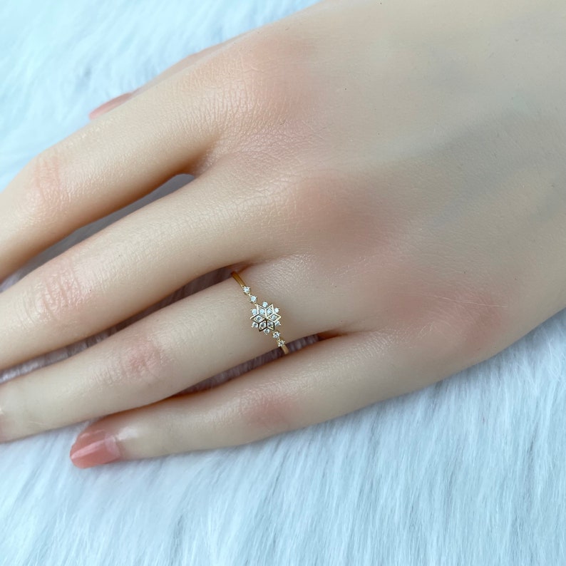 May include: A delicate gold ring with a snowflake design featuring small sparkling diamonds.