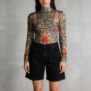 Pode incluir: Uma blusa transparente de manga comprida e gola alta com um padrão floral colorido, combinada com calções de ganga pretos. A blusa apresenta um decote alto e um design vibrante com tons de vermelho, amarelo, azul e verde. Os calções têm um design clássico.