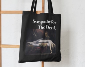Op de afbeelding: Zwarte tote bag met witte tekst die "Sympathie voor de Duivel" luidt. De tas heeft een zwart-witte afbeelding van een schilderij.