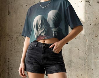 Puede incluir: Una camiseta corta azul oscuro con una pintura surrealista de dos figuras con rostros cubiertos. La modelo lleva pantalones cortos vaqueros negros y zapatillas de plataforma negras. El fondo es una pared de hormigón.