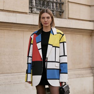 Könnte beinhalten: Ein farbblockartiger Blazer im Mondrian-Stil mit roten, gelben, blauen und schwarzen geometrischen Formen, die mit Schwarz umrandet sind. Der Blazer wird mit einem schwarzen Outfit und schwarzen Schuhen getragen. Eine kleine schwarze Handtasche ist ebenfalls zu sehen.