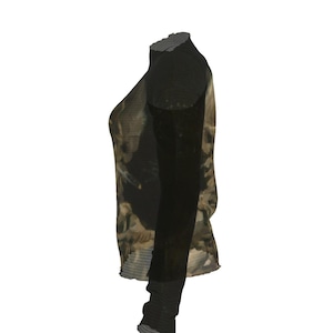 Puede incluir: Una camiseta de manga larga con cuello alto. Las mangas y el cuello son negros, mientras que el cuerpo de la camiseta presenta un dise&ntilde;o apagado y estampado en tonos marr&oacute;n, beige y verde oliva. La tela parece ser semitransparente.