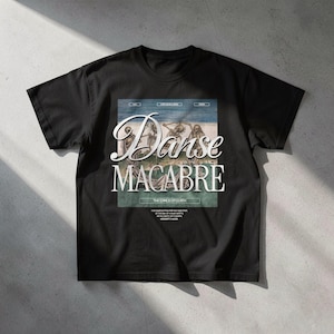 Puede incluir: Una camiseta negra de manga corta con un estampado gráfico central de esqueletos bailando. El texto dice Danse Macabre, The Dance of Death, e incluye líneas de texto más pequeñas debajo de la ilustración en una paleta de colores blanco y gris.