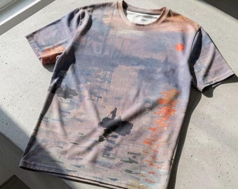 May include: A short-sleeve crew neck t-shirt featuring an all-over print of an impressionist painting depicting a harbor scene at sunset with a small boat, dark silhouettes of structures, and a bright orange sun reflecting on the water.