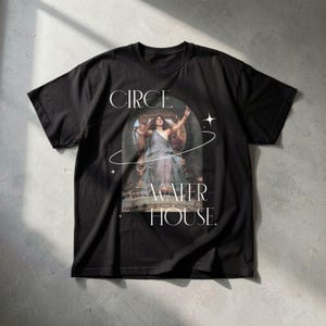 Puede incluir: Camiseta negra con estampado de arte clásico. El diseño incluye el texto "CIRCE. WATER HOUSE" y una imagen de una mujer con un vestido fluido con los brazos extendidos, enmarcada en un arco. Texto blanco y gráficos de estrellas.