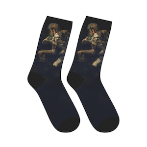 Puede incluir: Un par de calcetines negros con una pintura oscura y surrealista de una criatura con una lengua larga y un objeto blanco. La obra de arte está impresa en la parte delantera de los calcetines, con talones y dedos negros.