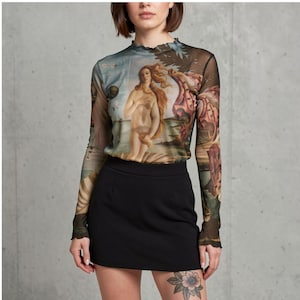 Puede incluir: Una blusa transparente de manga larga con un estampado de pintura renacentista, combinada con una minifalda negra. La blusa presenta una figura desnuda clásica. La falda es de color negro liso.