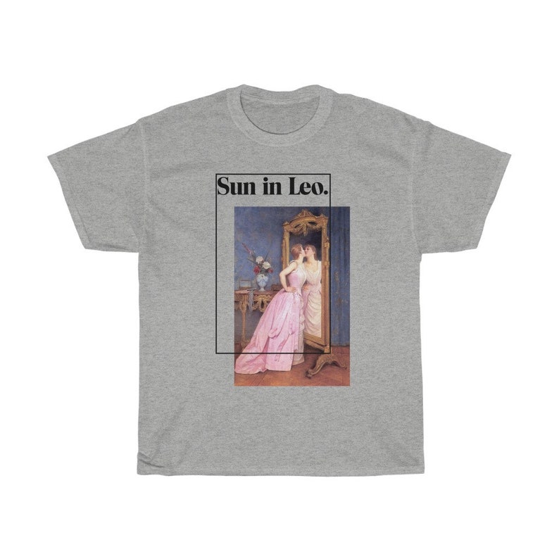 Puede incluir: Camiseta gris con una imagen enmarcada de una mujer con un vestido rosa mir&aacute;ndose en un espejo. El texto "Sun in Leo." est&aacute; encima de la imagen en un rect&aacute;ngulo negro.