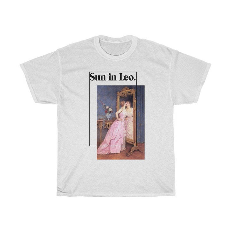 Puede incluir: Camiseta blanca con una imagen enmarcada de dos mujeres, una con un vestido rosa, reflejadas en un espejo. El texto "Sun in Leo." est&aacute; encima de la imagen. La camiseta es de estilo unisex.