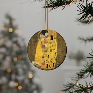Puede incluir: Adorno navideño redondo con la obra "El Beso" de Gustav Klimt. El adorno tiene una cuerda dorada para colgar. La obra representa a una pareja abrazándose, con tonos dorados, amarillos y negros. El fondo es dorado apagado.