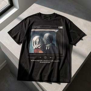May include: Black t-shirt with a print of a couple with shrouded faces, inspired by René Magritte's "The Lovers." The print includes the text "Les Amants" and a French quote. The shirt is made of a soft material.
