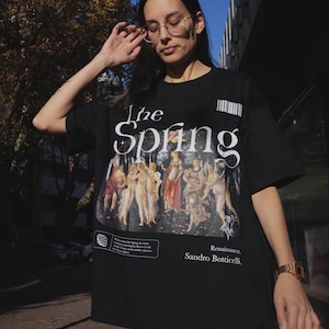 Puede incluir: Camiseta negra con un estampado gráfico de la pintura "El nacimiento de Venus" de Sandro Botticelli. El texto "The Spring" está impreso sobre la imagen y "Renaissance. Sandro Botticelli." está impreso debajo de la imagen.