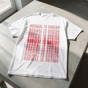 Puede incluir: Camiseta blanca con la frase "NORMAL IS BORING" en rojo repetida. El texto se repite vertical y horizontalmente en la camiseta. La camiseta está hecha de un material suave.