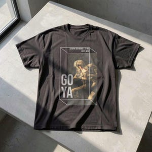 Könnte beinhalten: Dunkelgraues T-Shirt mit einem Druck von Goyas 'Saturn verschlingt seinen Sohn', mit dem Text 'GO YA' in Weiß. Das Kunstwerk ist in einem weißen Rahmen eingefasst, und das T-Shirt enthält den Text 'SEGUNDO DEBORANDO A SU HIJO (1821-1823)'.