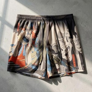 Puede incluir: Shorts de malla con cintura con cordón. Los shorts presentan un diseño de inspiración japonesa con geishas, ​​calaveras y obras de arte tradicionales en beige, negro, rojo y azul.