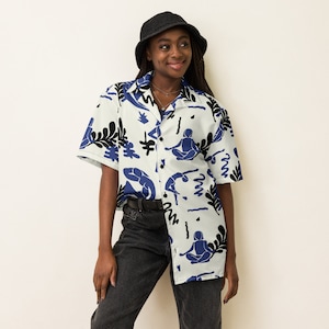 Può includere: Una camicia bianca con bottoni, maniche corte e una stampa astratta blu e nera. La stampa presenta figure stilizzate in una posa yoga e forme astratte.