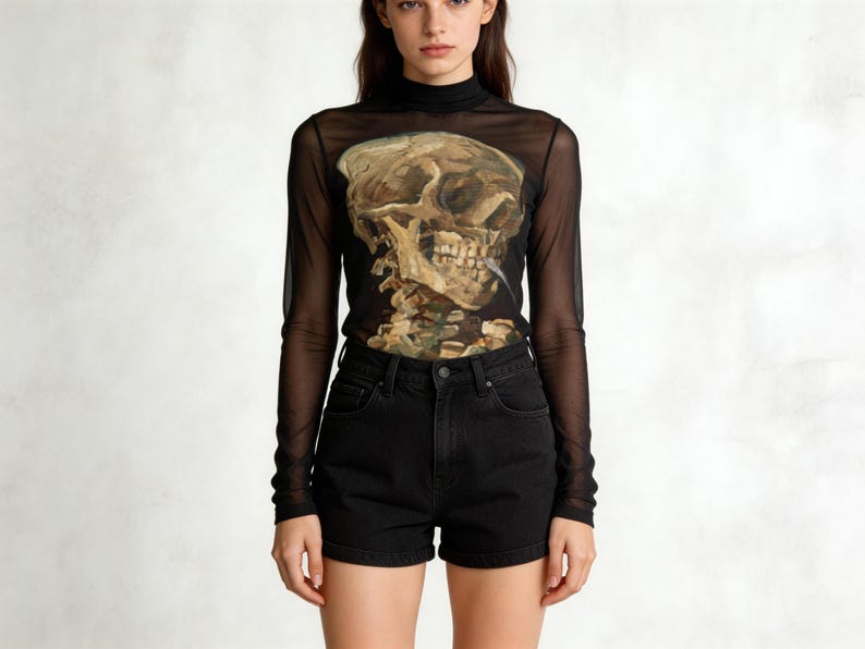 Puede incluir: Top negro de manga larga de malla con un gr&aacute;fico de calavera y pantalones cortos de mezclilla negros. El gr&aacute;fico de la calavera est&aacute; detallado con tonos marrones y beige. El top tiene un cuello alto.