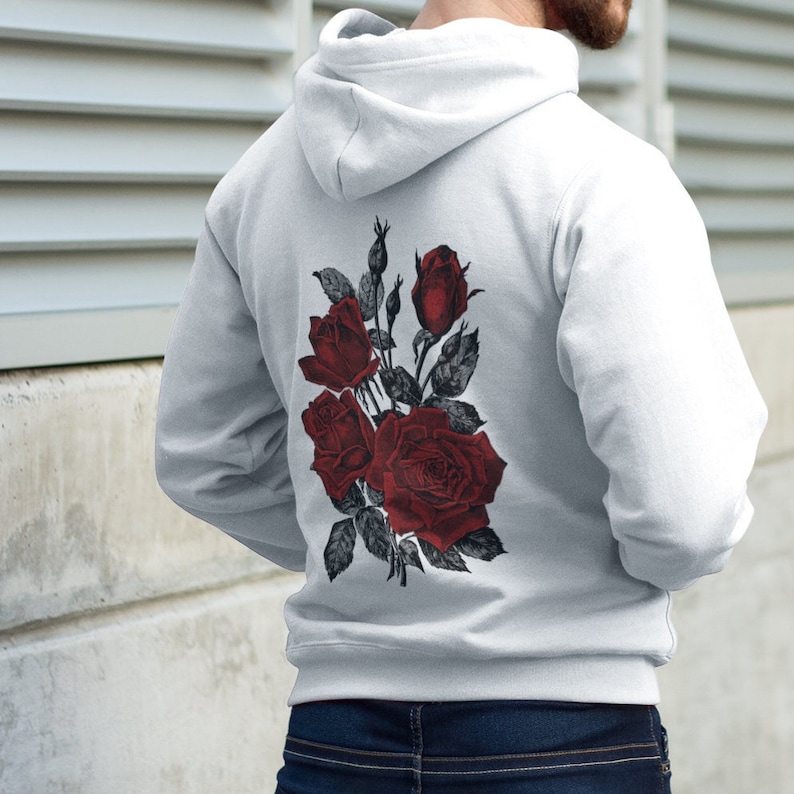 May include: A white hoodie with a red rose print on the back. The roses are arranged in a bouquet with green leaves.