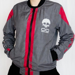 May include: Grey bomber jacket with red stripes and a skull graphic. The jacket has a black zip, collar, and cuffs. The text "99" is below the skull. The jacket is made of a lightweight material.