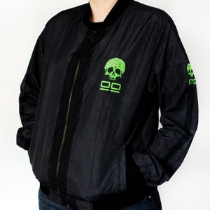 May include: Black bomber jacket with a green skull and double bars graphic on the front and a smaller skull graphic on the sleeve.