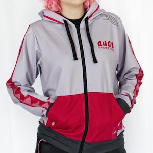 May include: A gray and red zip-up hoodie with a hood and pockets. The hoodie features red accents on the sleeves and a red lower section. The text "audd KasaneTeto" is printed on the chest. The hoodie has black drawstrings and a black zipper.